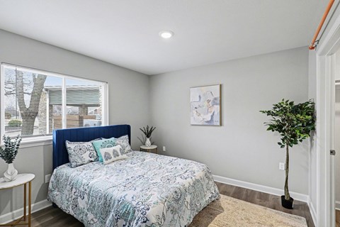 A bedroom with a bed, a plant, and a painting on the wall at Mayfair Apartments, Kansas City