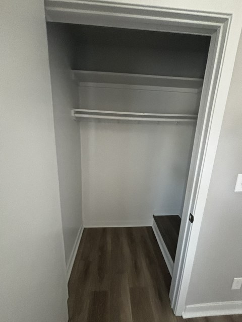 a walk in closet in a home with white walls and wood floors