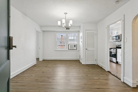 A large empty room with a chandelier and a kitchen in the background. at Shipyard Shores Apartments, Newport News, 23607