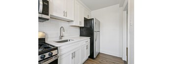 A black refrigerator is in a kitchen with white cabinets.
