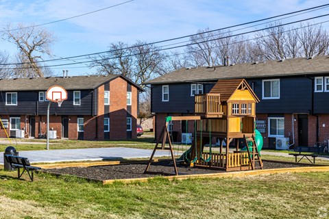 A playground with a basketball hoop and a wooden swing set.