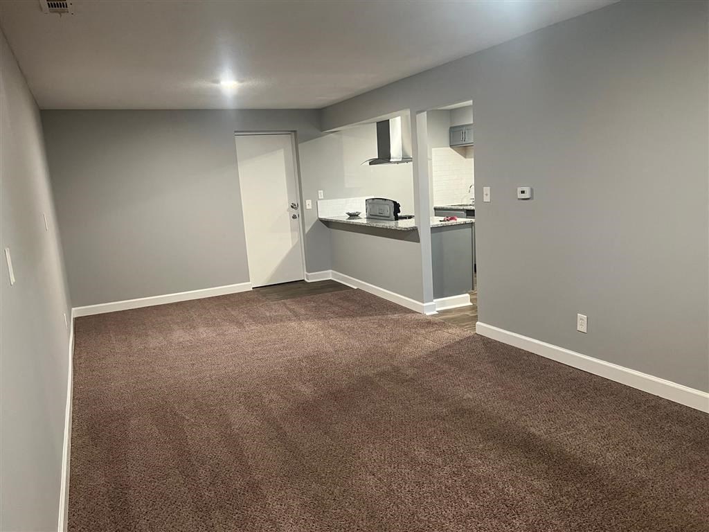 a living room with a carpet and a kitchen