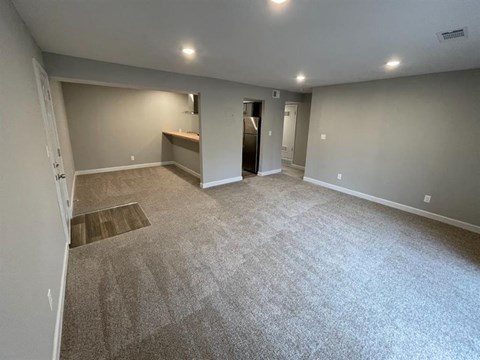 a empty living room with carpet and a kitchen