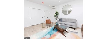 A living room with a grey couch, a brown chair, a glass coffee table and a blue rug.