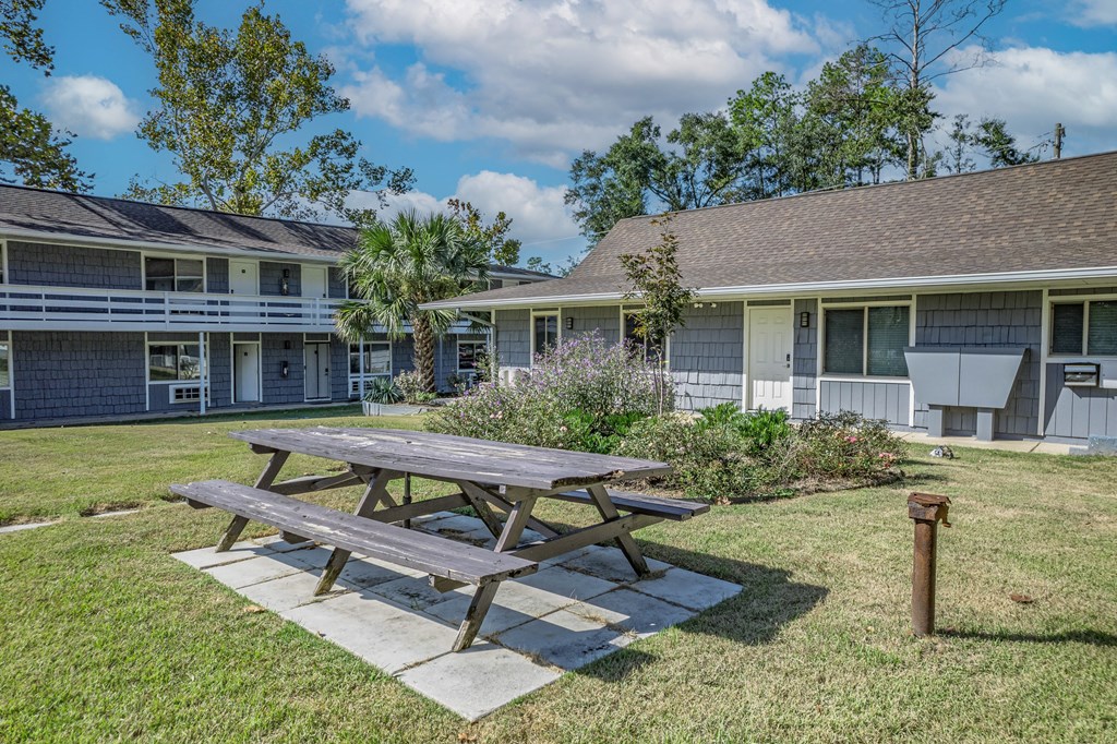 A picnic table is in the middle of a grassy area in front of a building.