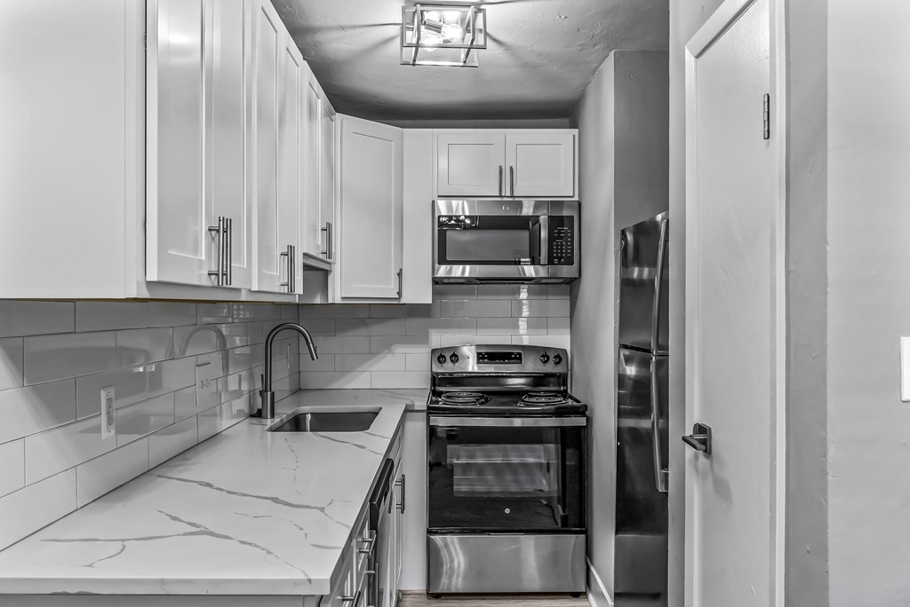 A black and white image of a kitchen with stainless steel appliances and white cabinets.