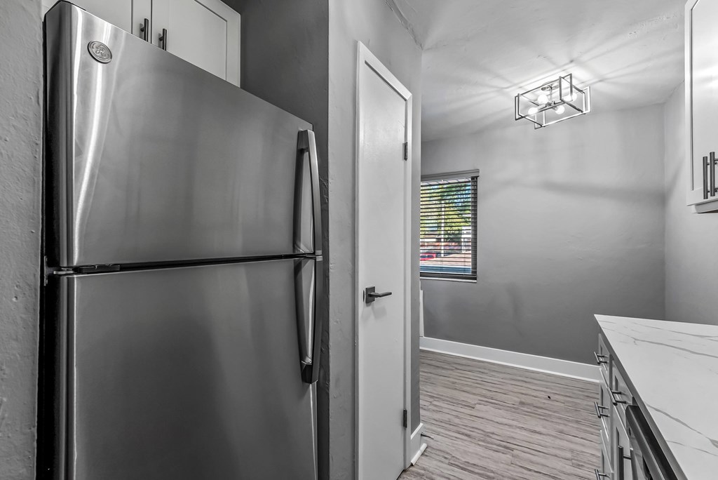 A stainless steel refrigerator stands in a kitchen with wood flooring.