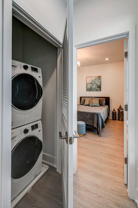 A white door is open to a bedroom with a bed and a painting on the wall.