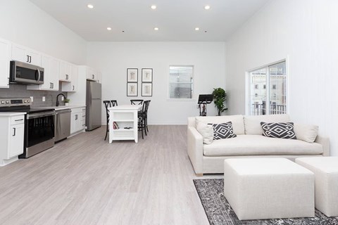A modern kitchen with a white color scheme and a living room with a white couch and ottoman.