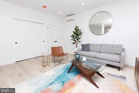 A living room with a grey couch, a brown chair, a glass coffee table and a blue rug.