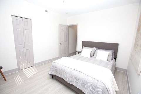 A bedroom with a bed, pillows, and a wooden floor.