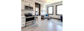 A modern kitchen with a stainless steel oven and microwave, a grey sofa, and a rug on the floor.