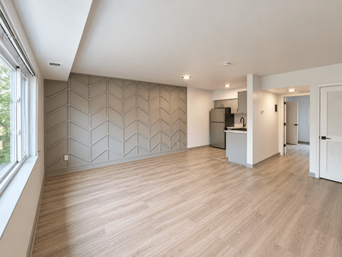 A spacious room with wooden flooring and a geometric patterned wall.