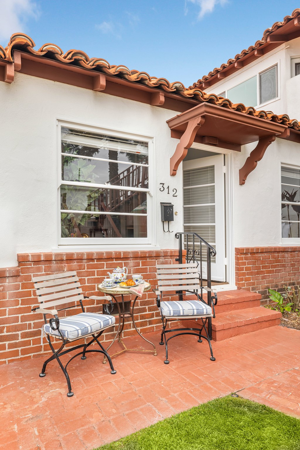 A patio with a table and two chairs in front of a house with the number 312 on it.
