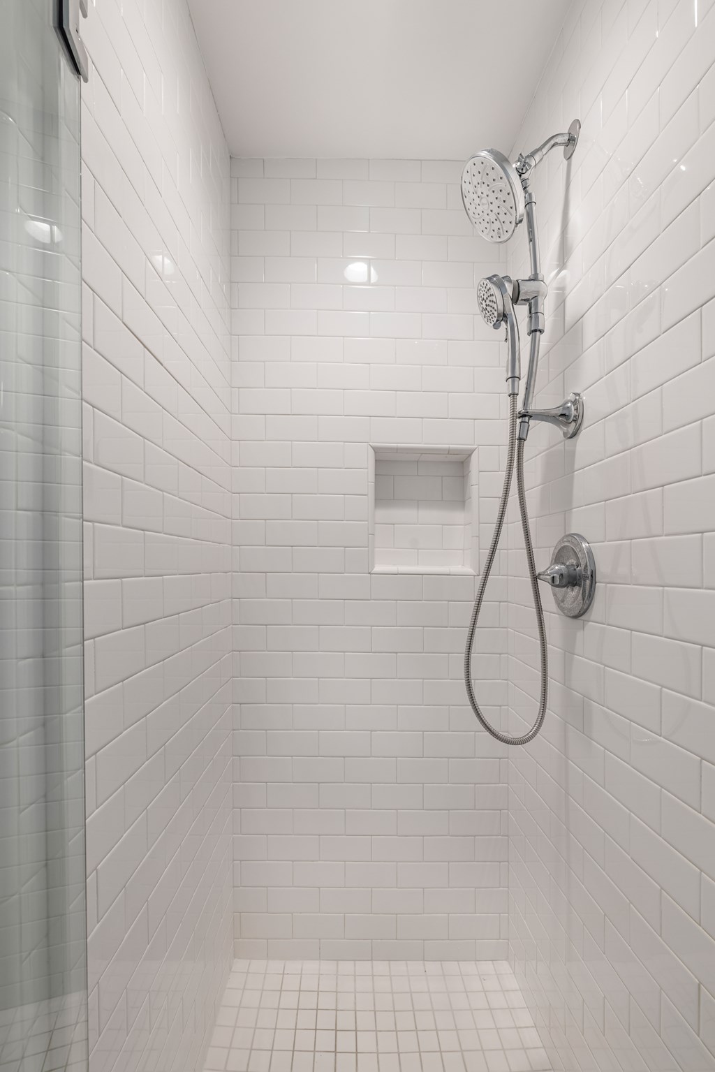 A white tiled shower with a shower head and hand held shower.