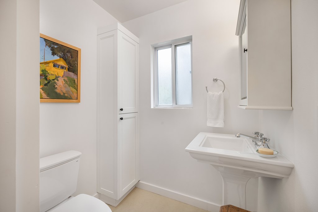 A white bathroom with a toilet, sink, and a painting on the wall.