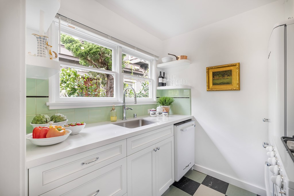 A kitchen with a white counter top and a window with plants on it.