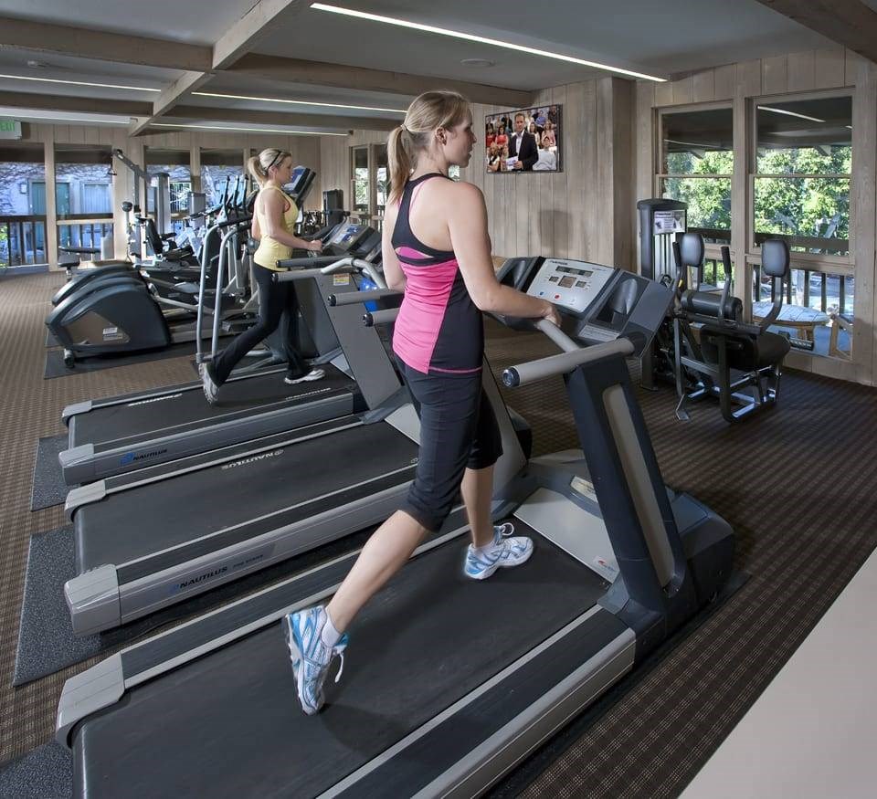a woman running on a treadmill in a gym at The Aspens Fairhaven, Santa Ana, CA