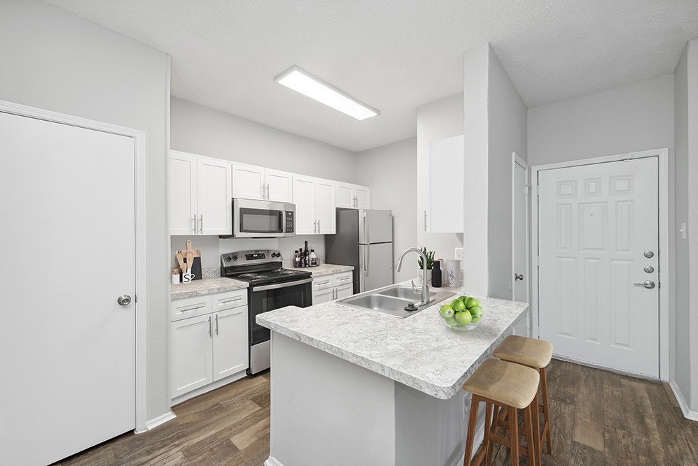 A kitchen with white cabinets and a marble island.