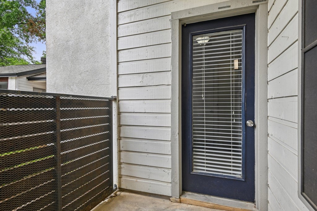 A blue door with a window above it and a fence to the left.