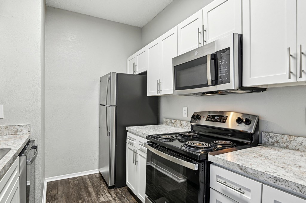 A kitchen with a black refrigerator, black stove, and white cabinets.