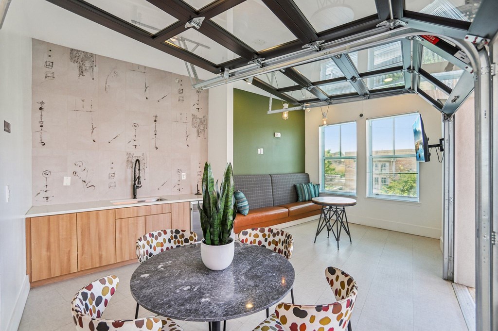 A room with a table and chairs in the foreground and a wall with drawings on it in the background.