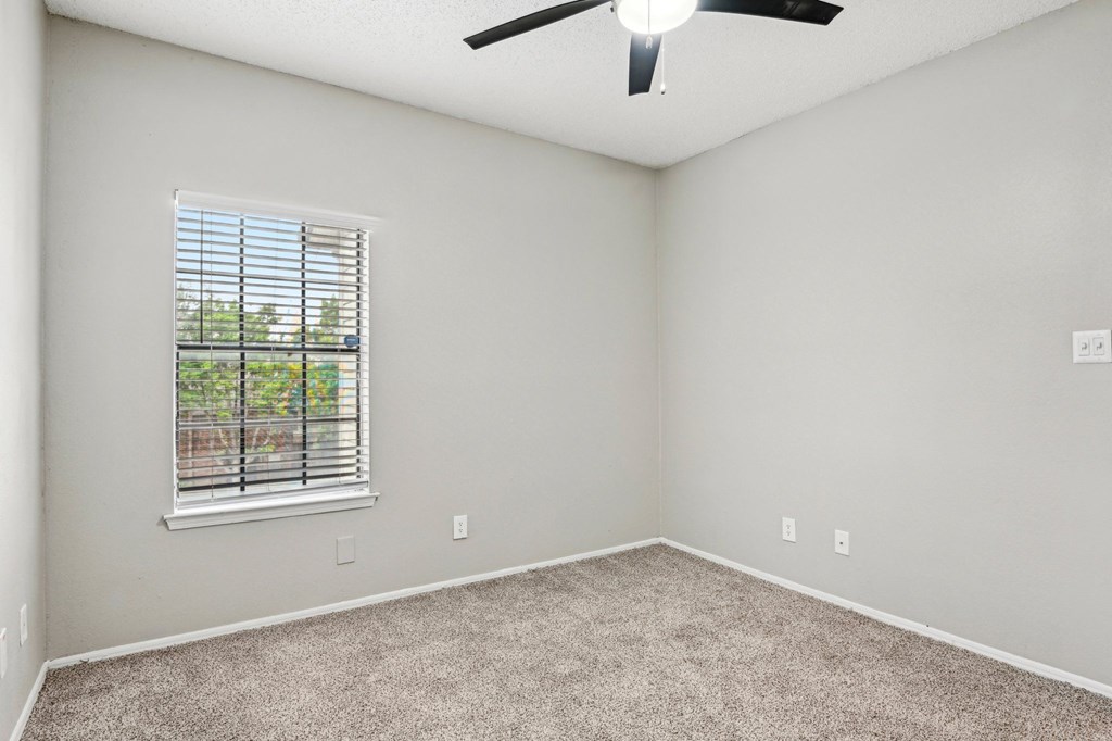 A room with a ceiling fan and a window with blinds.