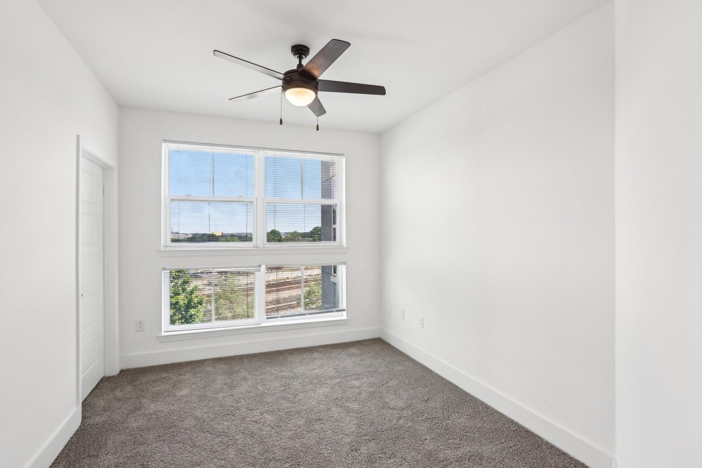 A room with a ceiling fan and a window overlooking a building.