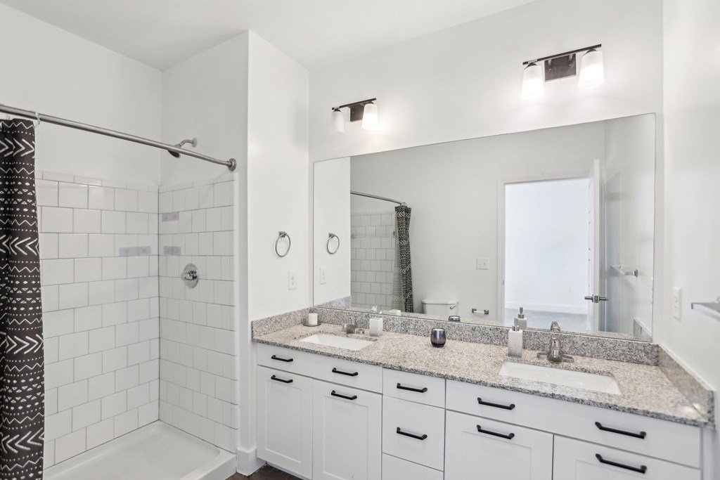A bathroom with a white tile shower and a marble countertop.