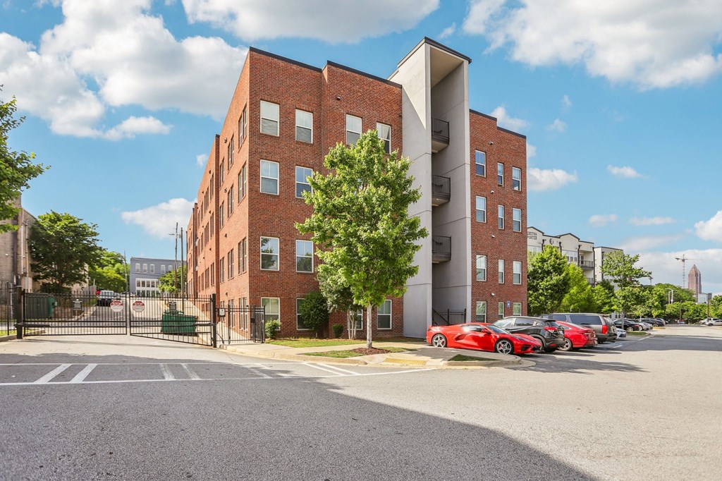 A red car is parked in a lot in front of a building.