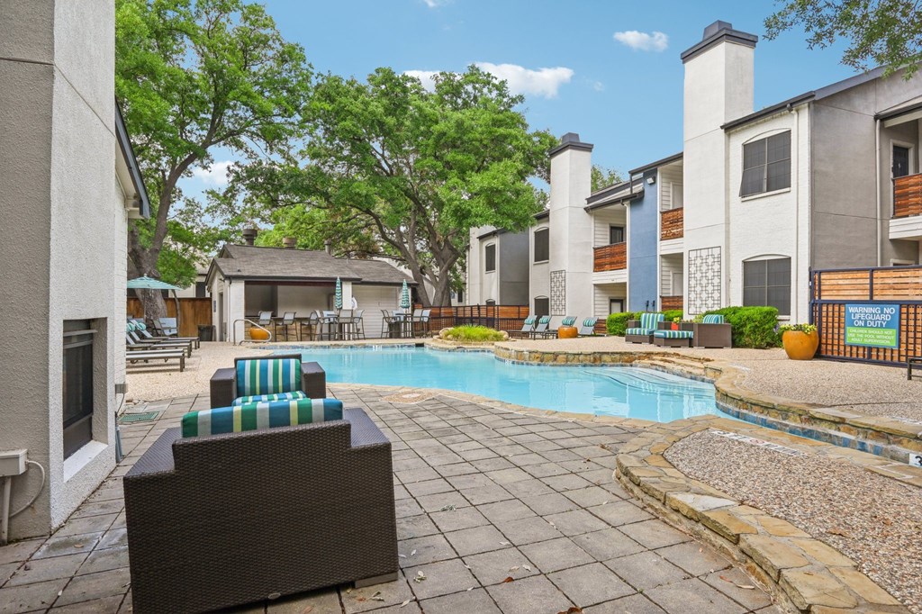 A pool surrounded by patio furniture and buildings.