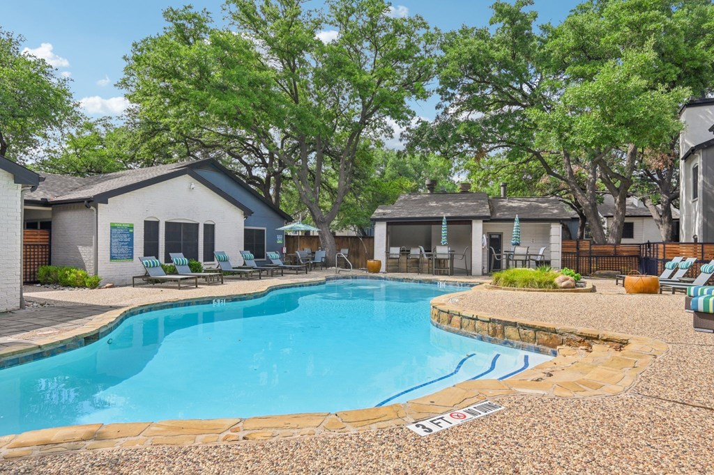 A pool surrounded by trees and chairs.