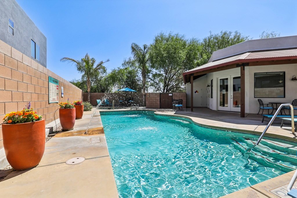 A pool with a waterfall and a patio area with chairs.