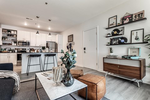 a living room with a table and a kitchen in the background