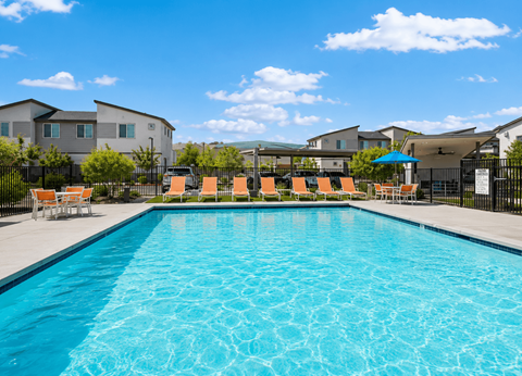 A swimming pool with orange chairs and a blue umbrella in front of a residential area.