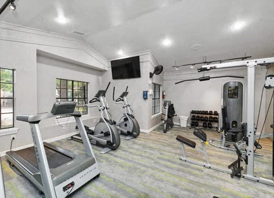a gym with exercise equipment and a tv on the wall at Heatherstone, Dallas
