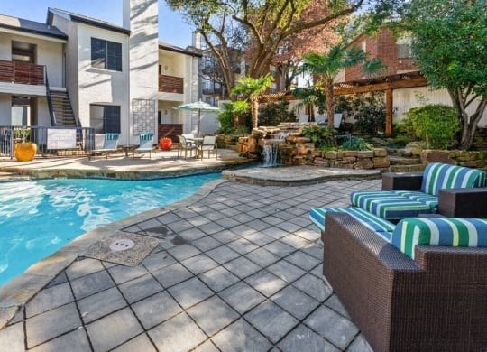 a swimming pool with chairs and umbrellas in front of a building at Heatherstone, Dallas, TX