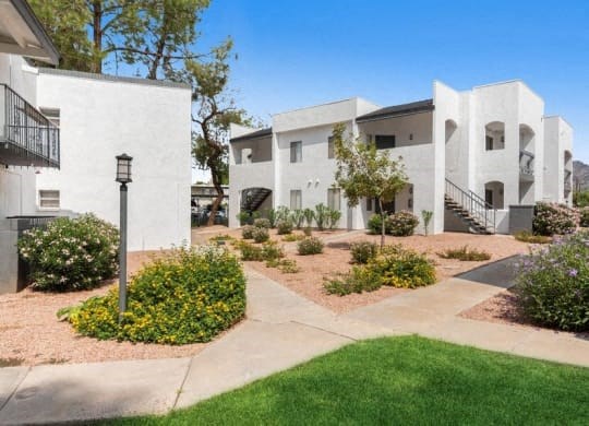 a group of white apartment buildings with a sidewalk and grass
