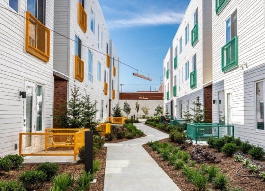 a walkway between two buildings with yellow benches and green plants at Marcato, Kansas City, 64108
