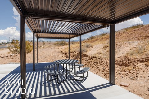 A metal patio structure with a table and chairs in a desert landscape.