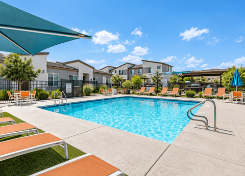 A swimming pool with orange lounge chairs and a green umbrella.