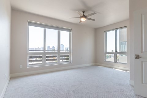 A spacious room with a ceiling fan and large windows overlooking a cityscape.