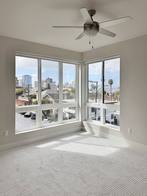 A room with a ceiling fan and large windows overlooking a cityscape.
