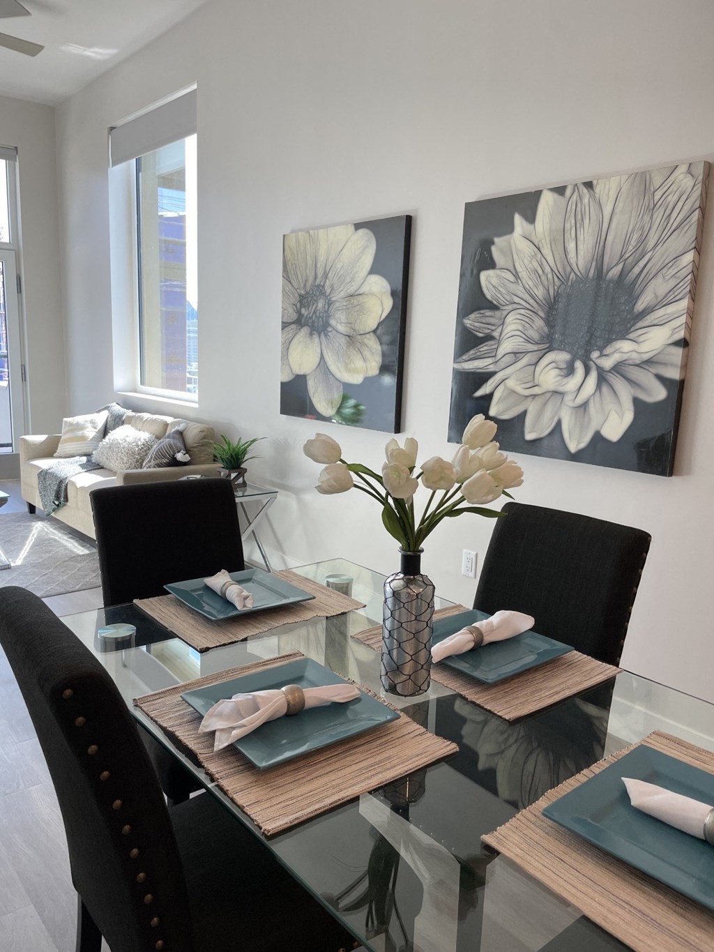 a dining room with a glass table and chairs and paintings on the wall