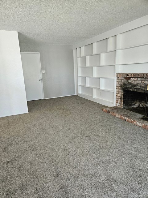 an empty living room with a fireplace and a carpeted floor