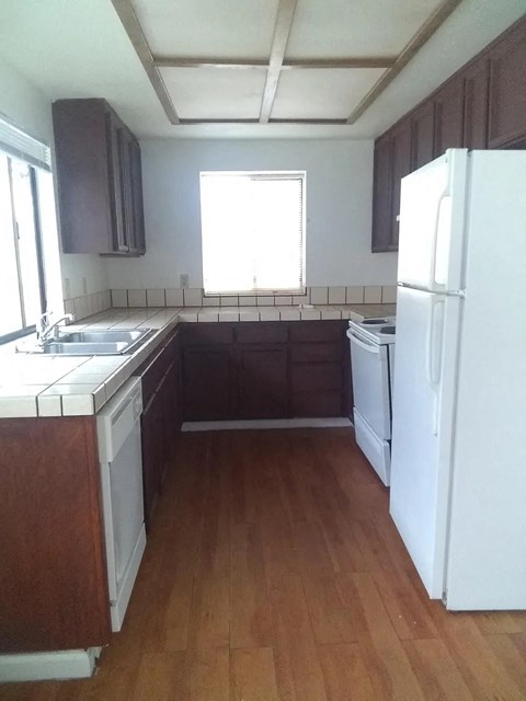 an empty kitchen with white appliances and wooden floors