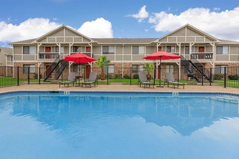 Swimming pool with lounge chairs and red umbrellas at Castlewood Apartments, Clute, 77531