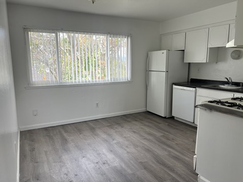 A kitchen with white appliances and a window with blinds.