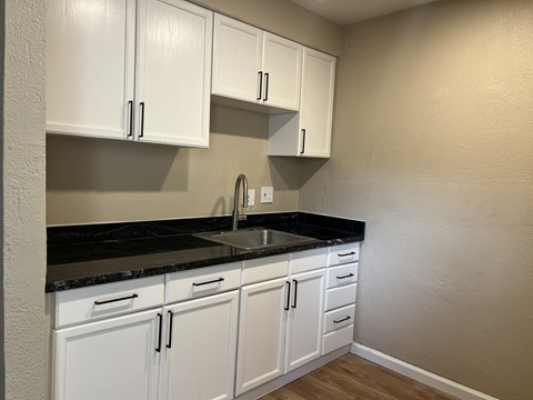 A kitchen with white cabinets and black countertops.
