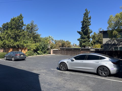 Two cars are parked in a parking lot with trees in the background.